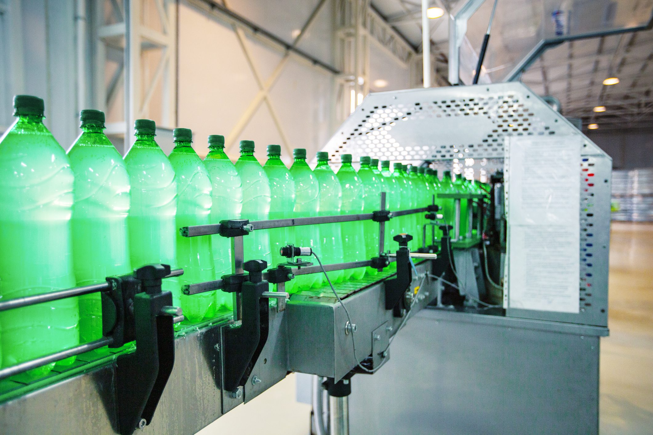 Green plastic bottles are being filled and capped on a conveyor belt at a manufacturing facility. This automated process highlights the efficiency of modern production lines.